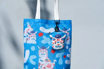 巷仔Niau水交社折疊托特包主商品展示照，將迷彩軍事元素轉化為印花圖案，並巧妙融入「水交社」字樣與配戴空軍帽的巷仔Niau角色，讓記憶以輕鬆可愛的方式走入日常生活。